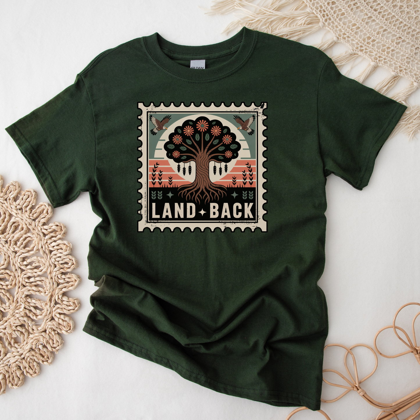 Green t-shirt with a tree graphic and 'Land Back' text on a white surface with decorative elements. land back shirt, indigenous awareness shirt, nature shirt, tree graphic tee, minimalist shirt, advocacy apparel, eco conscious clothing, indigenous inspired apparel, social justice shirt, unisex t shirt, earthy aesthetic clothing, statement tee