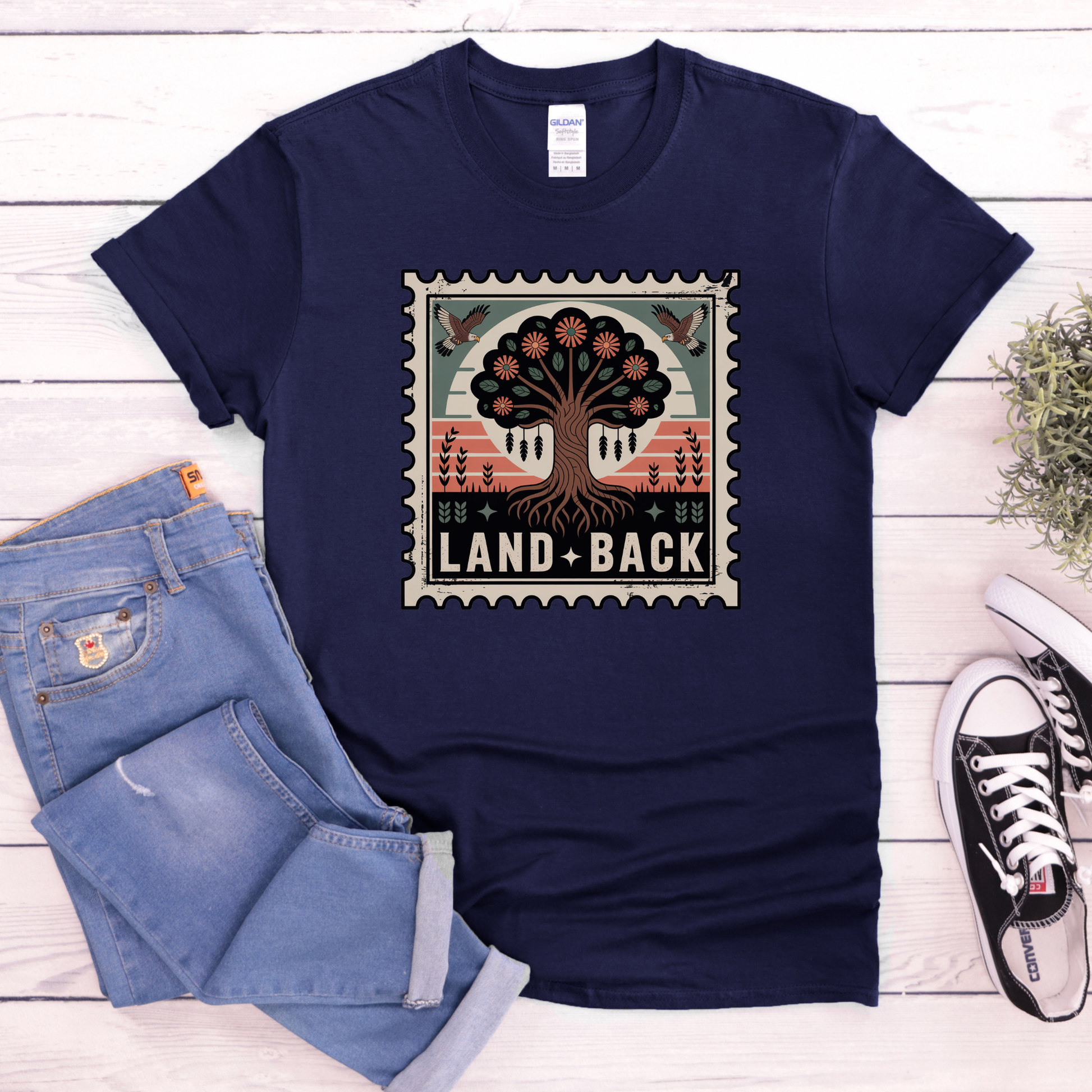 Navy blue t-shirt with a graphic design and text, paired with jeans and sneakers on a wooden surface. land back shirt, indigenous awareness shirt, nature shirt, tree graphic tee, minimalist shirt, advocacy apparel, eco conscious clothing, indigenous inspired apparel, social justice shirt, unisex t shirt, earthy aesthetic clothing, statement tee