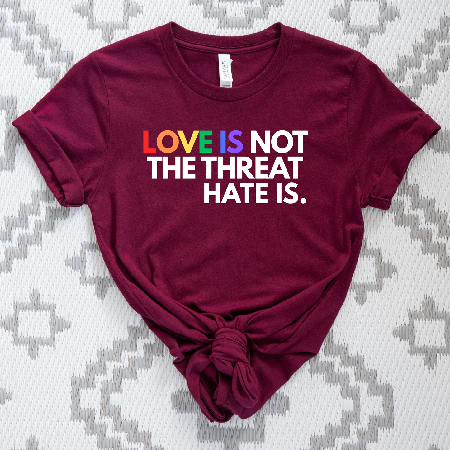t-shirt featuring the phrase "Love Is Not The Threat Hate Is." with rainbow-colored lettering for Love, promoting LGBTQ+ pride, equality, and inclusion. love is not the threat hate is shirt, pride shirt, pride ally shirt, LGBTQ shirt, LGBTQ ally, equality shirt, love wins shirt, rainbow shirt, inclusive apparel, human rights shirt, kindness shirt, acceptance shirt, pride month shirt, ally gift, social justice shirt, equality tee, progressive apparel, support LGBTQ, activist shirt, inclusive graphic tee