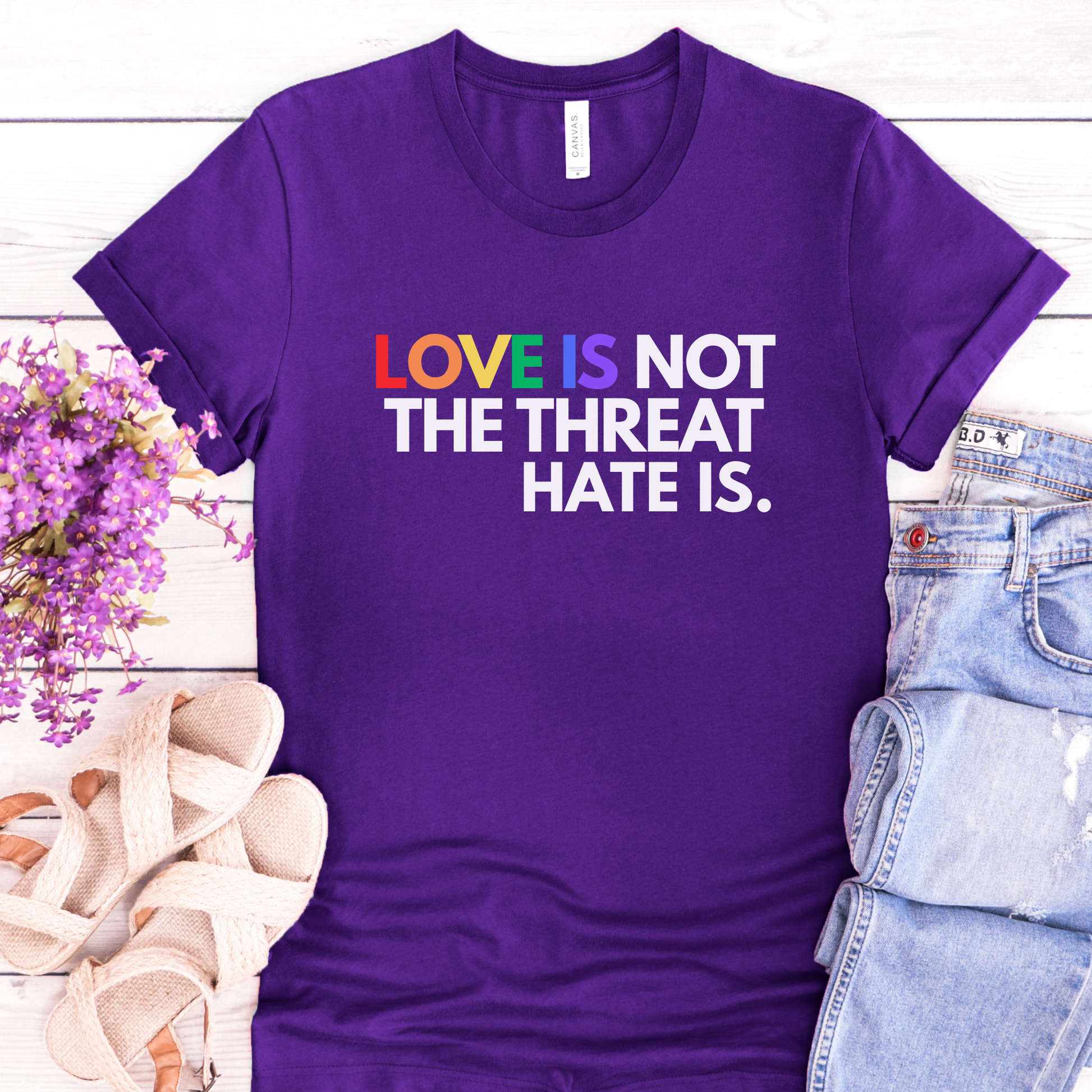 t-shirt featuring the phrase "Love Is Not The Threat Hate Is." with rainbow-colored lettering for Love, promoting LGBTQ+ pride, equality, and inclusion. love is not the threat hate is shirt, pride shirt, pride ally shirt, LGBTQ shirt, LGBTQ ally, equality shirt, love wins shirt, rainbow shirt, inclusive apparel, human rights shirt, kindness shirt, acceptance shirt, pride month shirt, ally gift, social justice shirt, equality tee, progressive apparel, support LGBTQ, activist shirt, inclusive graphic tee