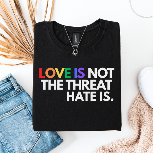 t-shirt featuring the phrase "Love Is Not The Threat Hate Is." with rainbow-colored lettering for Love, promoting LGBTQ+ pride, equality, and inclusion. love is not the threat hate is shirt, pride shirt, pride ally shirt, LGBTQ shirt, LGBTQ ally, equality shirt, love wins shirt, rainbow shirt, inclusive apparel, human rights shirt, kindness shirt, acceptance shirt, pride month shirt, ally gift, social justice shirt, equality tee, progressive apparel, support LGBTQ, activist shirt, inclusive graphic tee
