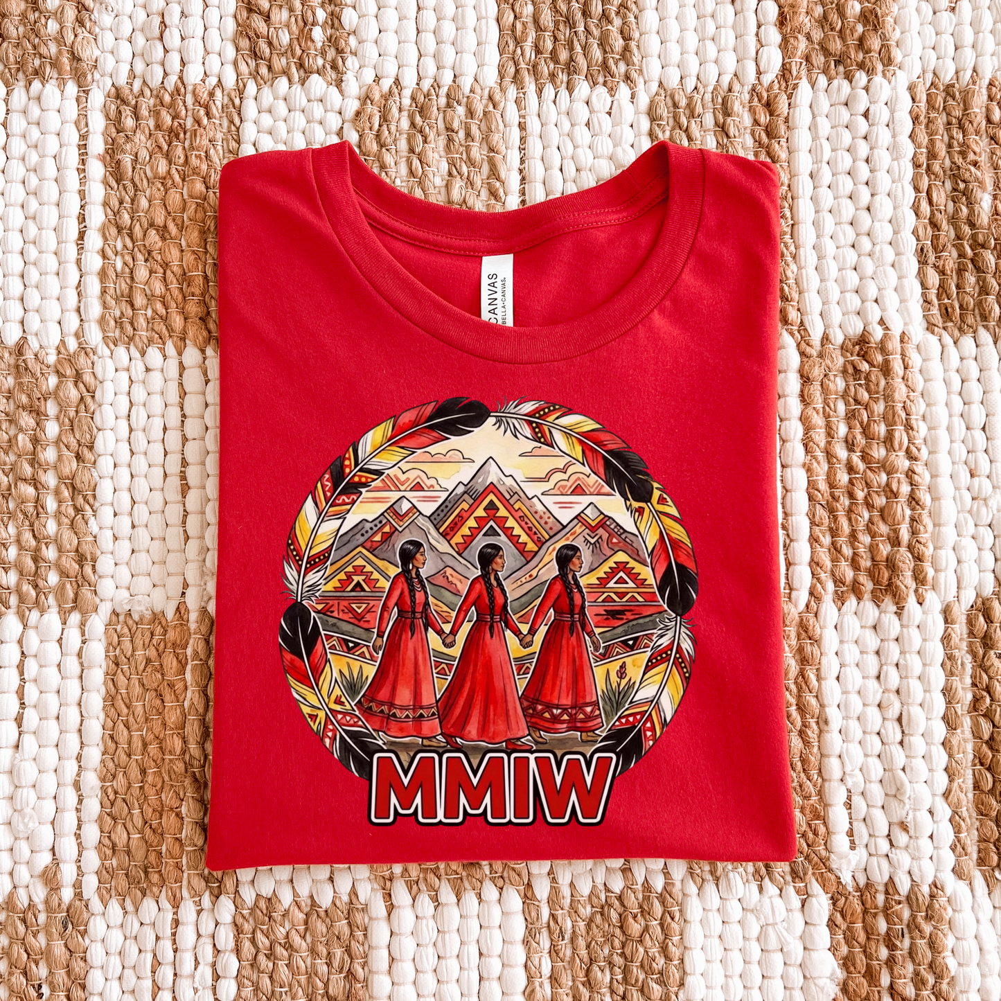 Red t-shirt with a graphic design and 'MMIW' text on a textured surface. The MMIW Feather Frame Unisex T-Shirt is a meaningful Indigenous awareness shirt designed to honor Missing and Murdered Indigenous Women, Girls, and Two-Spirit people. MMIW shirt, MMIW awareness, Indigenous t shirt, Missing and Murdered Indigenous Women, Indigenous graphic tee, Indigenous awareness shirt, unisex t shirt, activism shirt, Indigenous justice, Two Spirit awareness, Native apparel, awareness tee, Indigenous owned brand, fea