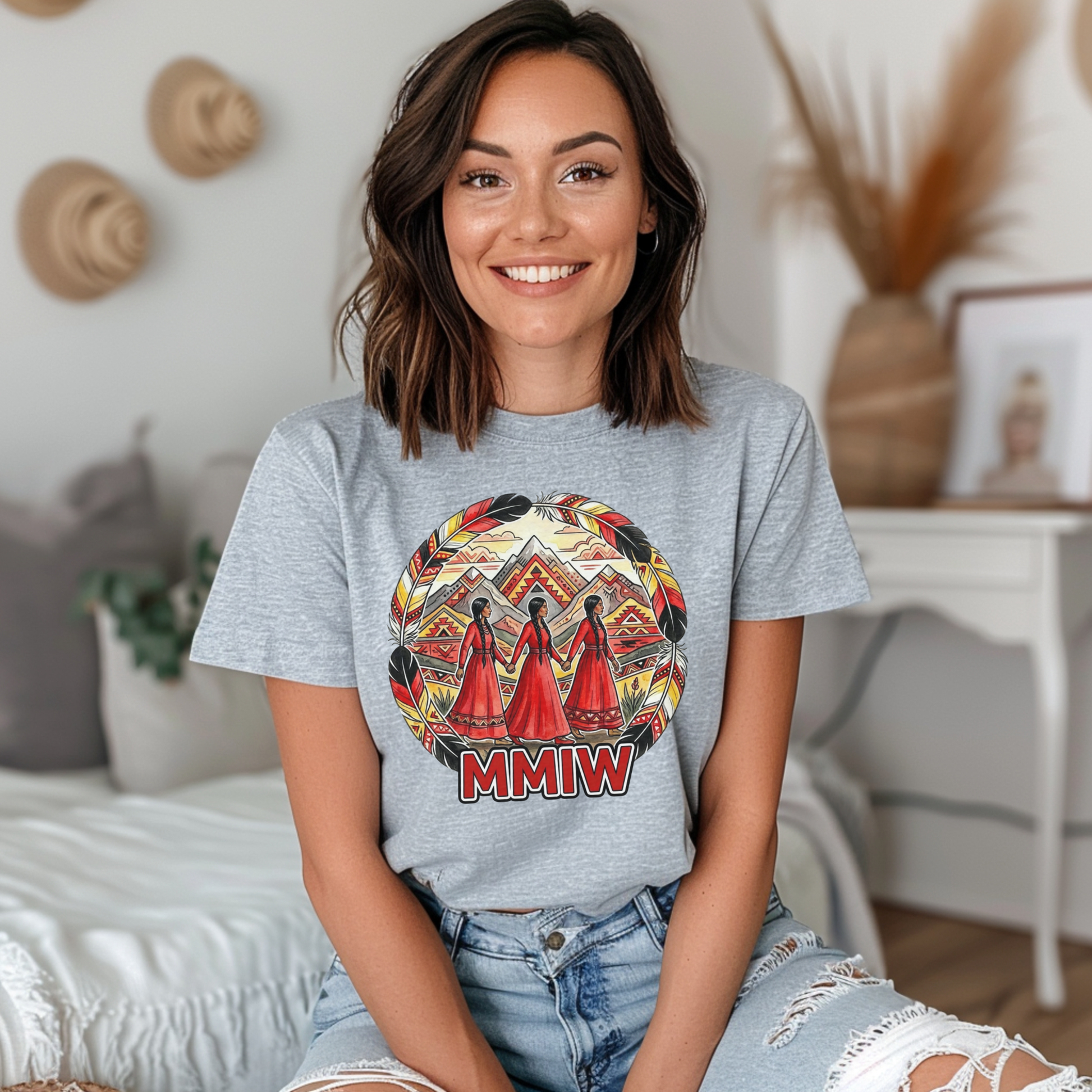 Woman wearing a gray t-shirt with a colorful graphic and 'MMIW' text, sitting in a cozy room. MMIW shirt, MMIW awareness, Indigenous t shirt, Missing and Murdered Indigenous Women, Indigenous graphic tee, Indigenous awareness shirt, unisex t shirt, activism shirt, Indigenous justice, Two Spirit awareness, Native apparel, awareness tee, Indigenous owned brand, feather frame shirt, statement t shirt