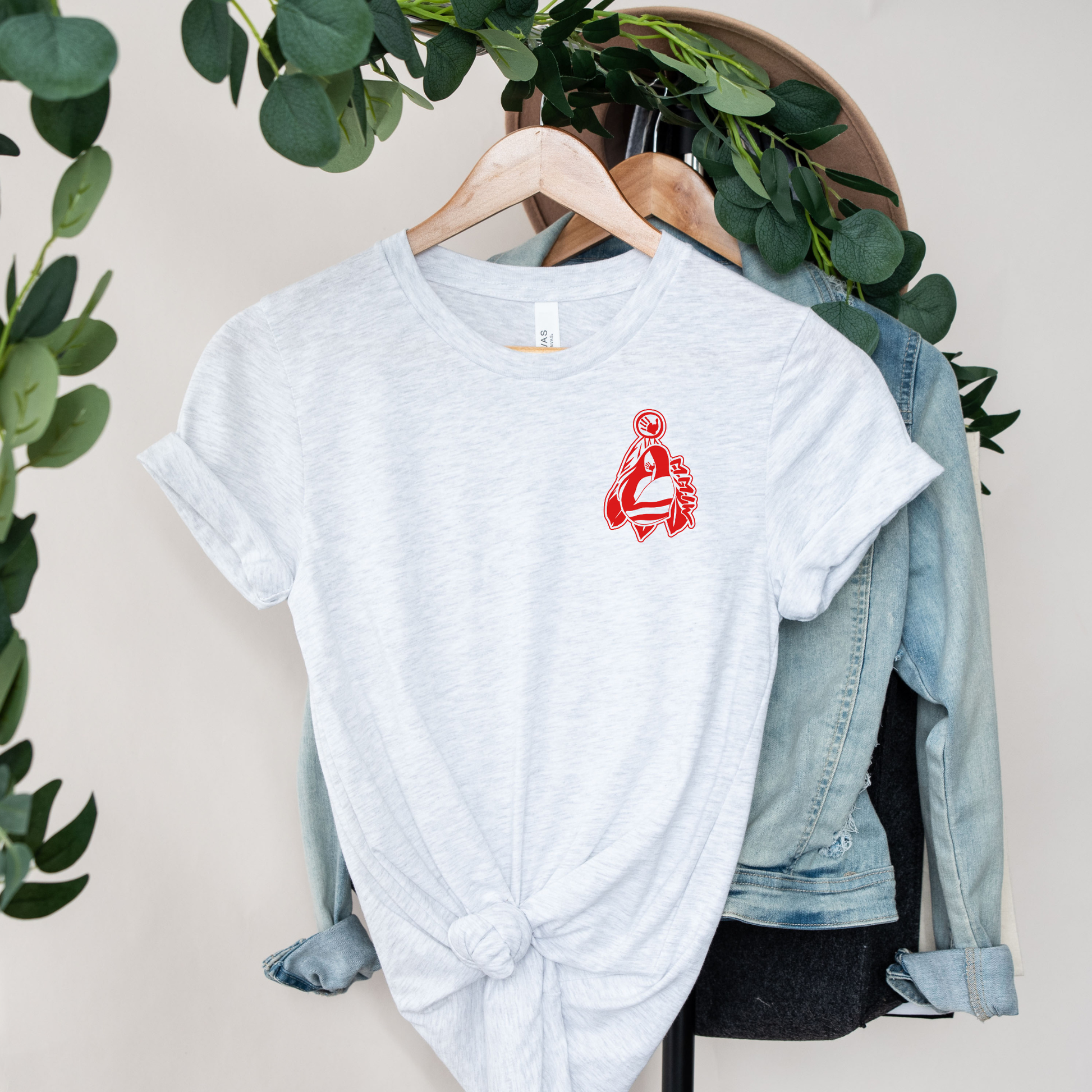 White t-shirt with red graphic on a hanger with a denim jacket and greenery in the background. MMIW shirt, MMIW woman in feathers, pocket design shirt, Indigenous awareness tee, Missing and Murdered Indigenous Women, Indigenous graphic tee, unisex t shirt, activism shirt, Indigenous justice, feather shirt, awareness apparel, Native shirt, statement tee, solidarity shirt, Indigenous owned brand