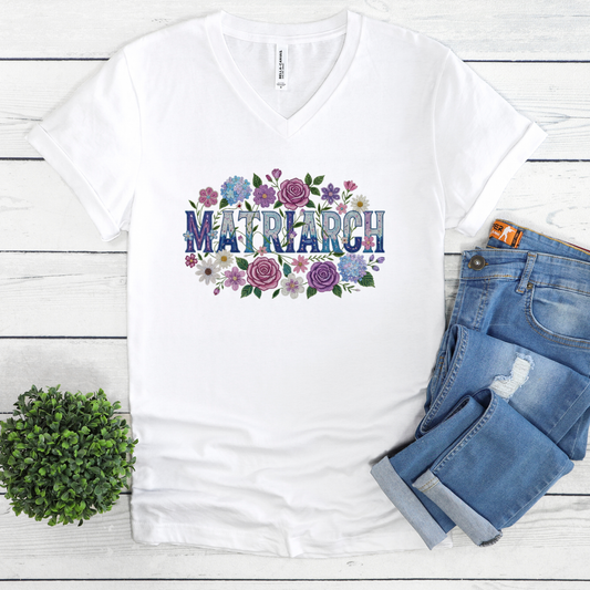 White t-shirt with 'Matriarch' design on a wooden surface with jeans and a plant. Indigenous Matriarch Shirt.