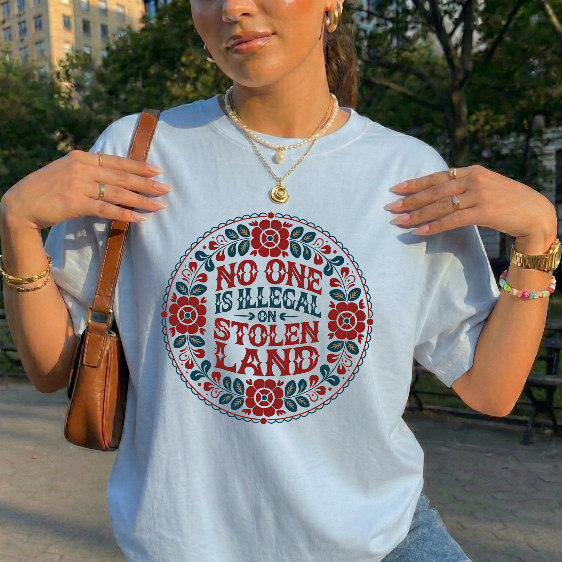 Person wearing a t-shirt with a floral design and text in an outdoor setting. No one is illegal on stolen land t-shirt, floral circle shirt, Indigenous floral tee, land back shirt, social justice t-shirt, stolen land circle design, activist floral apparel, Indigenous owned t-shirt, Sahdeh Spruce design, unisex activist tee, decolonization clothing, retro floral shirt, ethical fashion, protest graphic tee