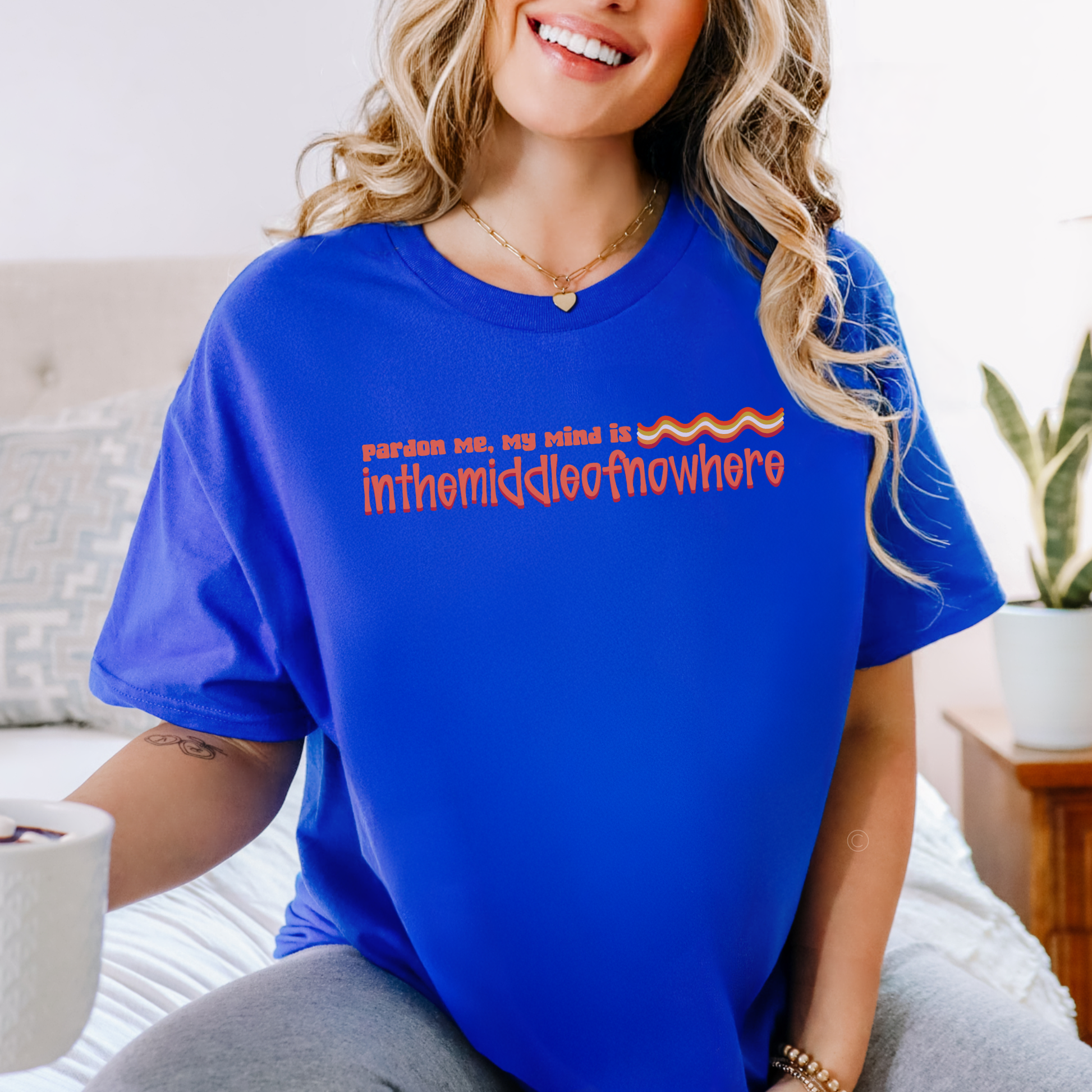 Woman wearing a blue t-shirt with text, sitting on a couch. funny quote shirt, sarcastic t shirt, unisex graphic tee, humor tee, funny saying shirt, casual quote shirt, statement tee, laid back shirt, daydreaming shirt, witty t shirt, gift idea shirt, funny unisex tee, everyday graphic tee, relaxed style shirt, humorous apparel