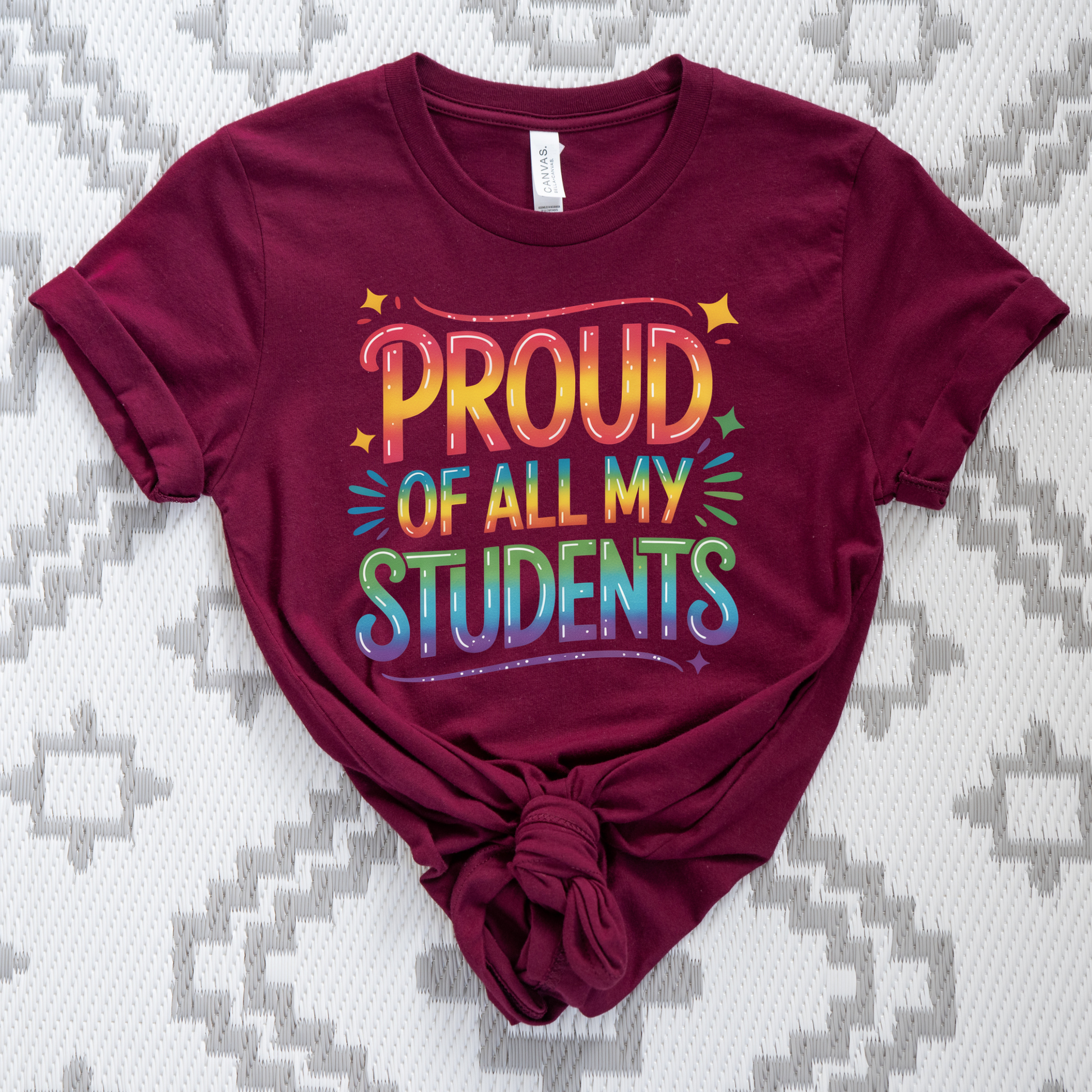 Maroon t-shirt with colorful text 'PROUD OF ALL MY STUDENTS' on a patterned background. teacher pride shirt, inclusive teacher shirt, LGBTQ ally teacher gift, pride month shirt, supportive teacher apparel, equality shirt for educators, school pride clothing, safe space shirt, diversity and inclusion tee, teacher appreciation gift, back to school pride shirt, unisex teacher shirt, classroom pride outfit, LGBTQ pride clothing, positive message shirt