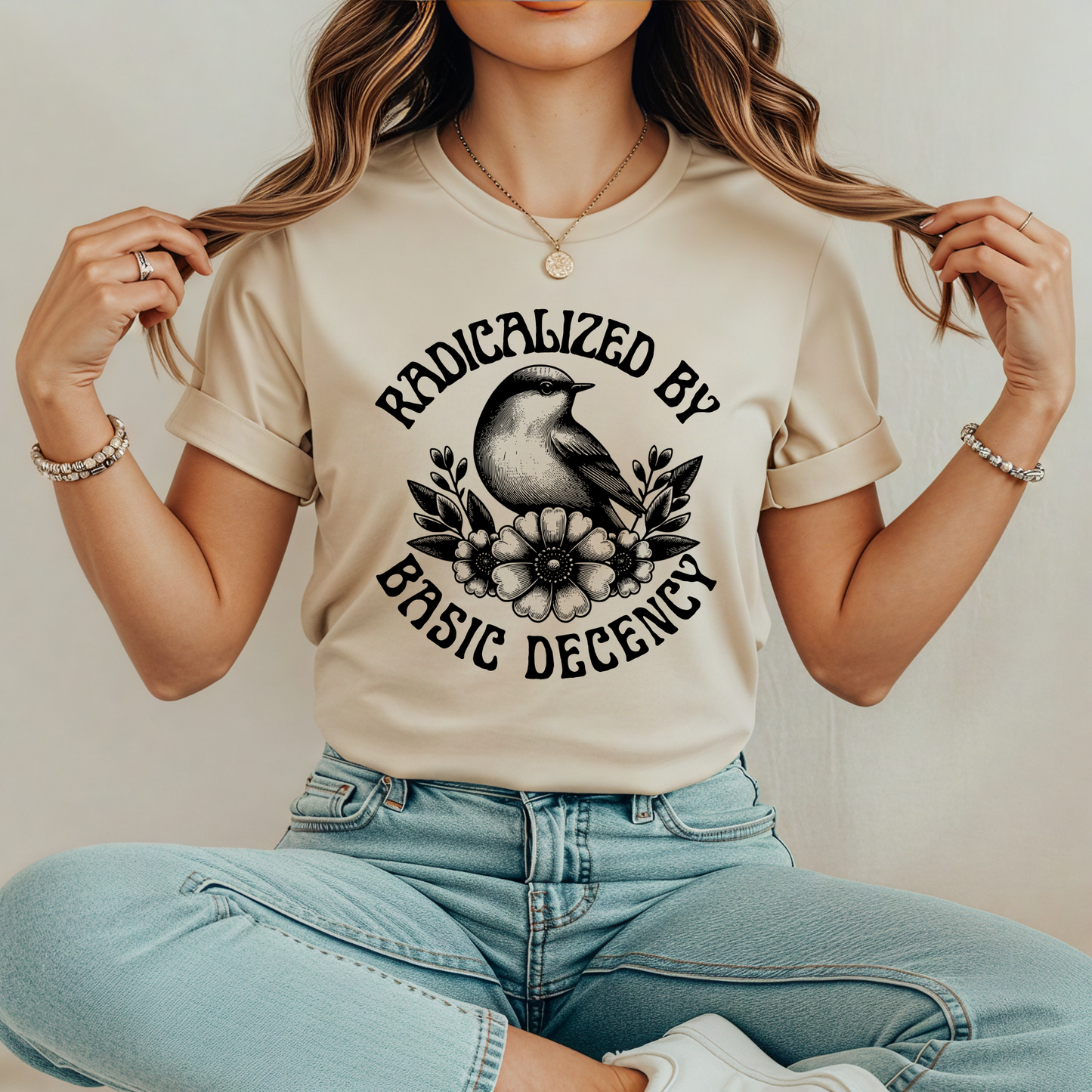 Person wearing a beige t-shirt with a graphic design and text, sitting against a neutral background. radicalized by basic decency shirt, progressive tee, activist shirt, social justice clothing, political statement tee, hypocrisy shirt, progressive apparel, rally shirt, protest tee, witty activist shirt, equality shirt, ally shirt, conversation starter tee, bold statement clothing, unisex political shirt