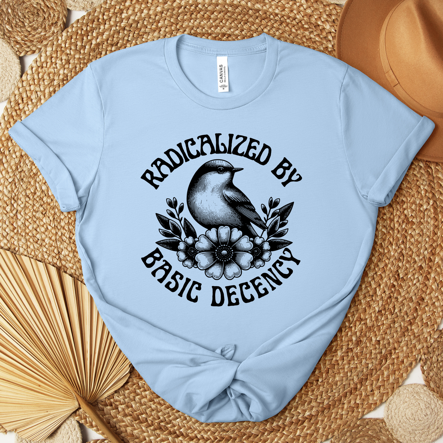 Light blue t-shirt with black graphic design and text on a woven surface. radicalized by basic decency shirt, progressive tee, activist shirt, social justice clothing, political statement tee, hypocrisy shirt, progressive apparel, rally shirt, protest tee, witty activist shirt, equality shirt, ally shirt, conversation starter tee, bold statement clothing, unisex political shirt