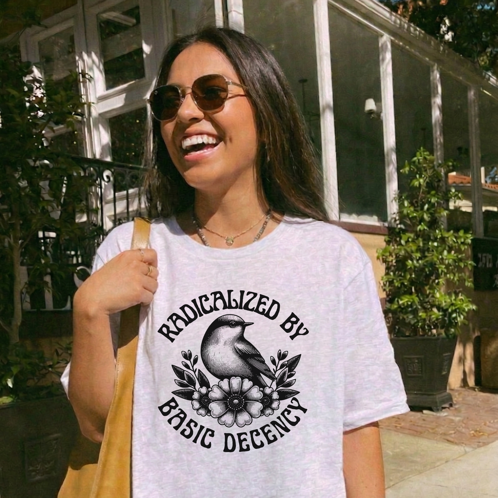 Woman wearing a white t-shirt with a graphic design and text, standing outdoors. radicalized by basic decency shirt, progressive tee, activist shirt, social justice clothing, political statement tee, hypocrisy shirt, progressive apparel, rally shirt, protest tee, witty activist shirt, equality shirt, ally shirt, conversation starter tee, bold statement clothing, unisex political shirt