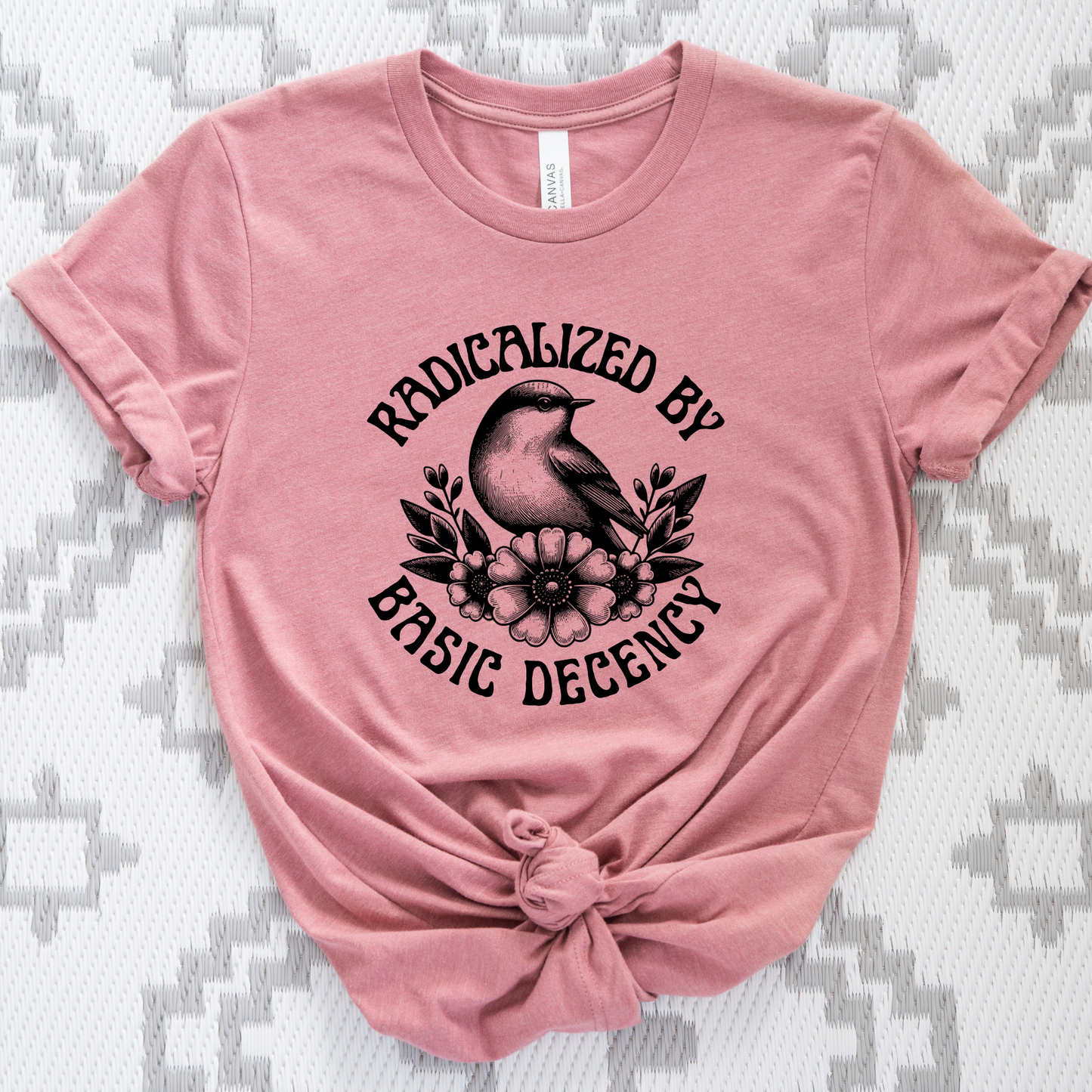 Pink t-shirt with black graphic and text on a textured gray background. radicalized by basic decency shirt, progressive tee, activist shirt, social justice clothing, political statement tee, hypocrisy shirt, progressive apparel, rally shirt, protest tee, witty activist shirt, equality shirt, ally shirt, conversation starter tee, bold statement clothing, unisex political shirt