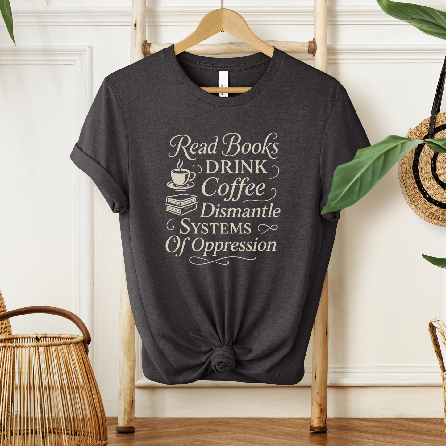 Black t-shirt with motivational text on a hanger against a neutral wall. read books drink coffee dismantle systems of oppression shirt, activist shirt, book lover shirt, coffee lover tee, social justice shirt, political statement tee, feminist shirt, progressive apparel, reader shirt, library shirt, protest shirt, anti oppression shirt, unisex graphic tee, outspoken clothing, education and activism shirt