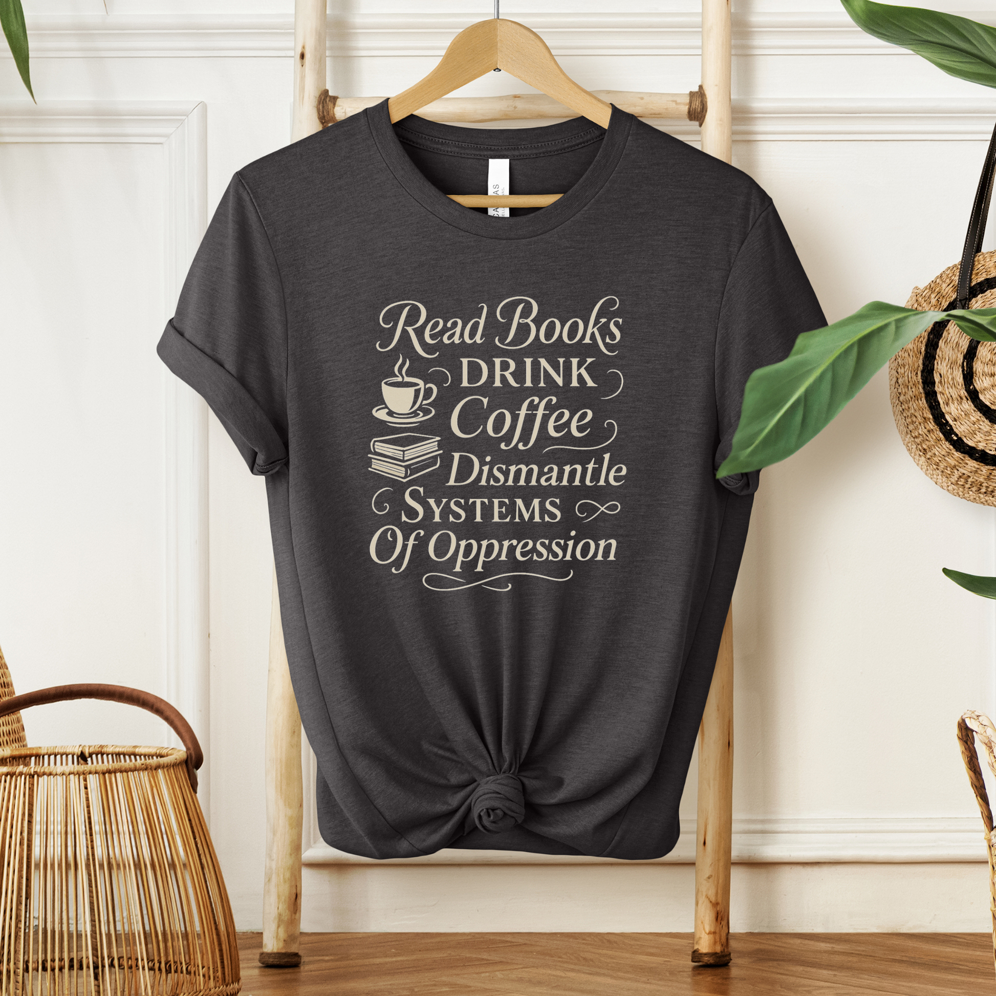 Black t-shirt with motivational text on a hanger against a neutral wall. read books drink coffee dismantle systems of oppression shirt, activist shirt, book lover shirt, coffee lover tee, social justice shirt, political statement tee, feminist shirt, progressive apparel, reader shirt, library shirt, protest shirt, anti oppression shirt, unisex graphic tee, outspoken clothing, education and activism shirt