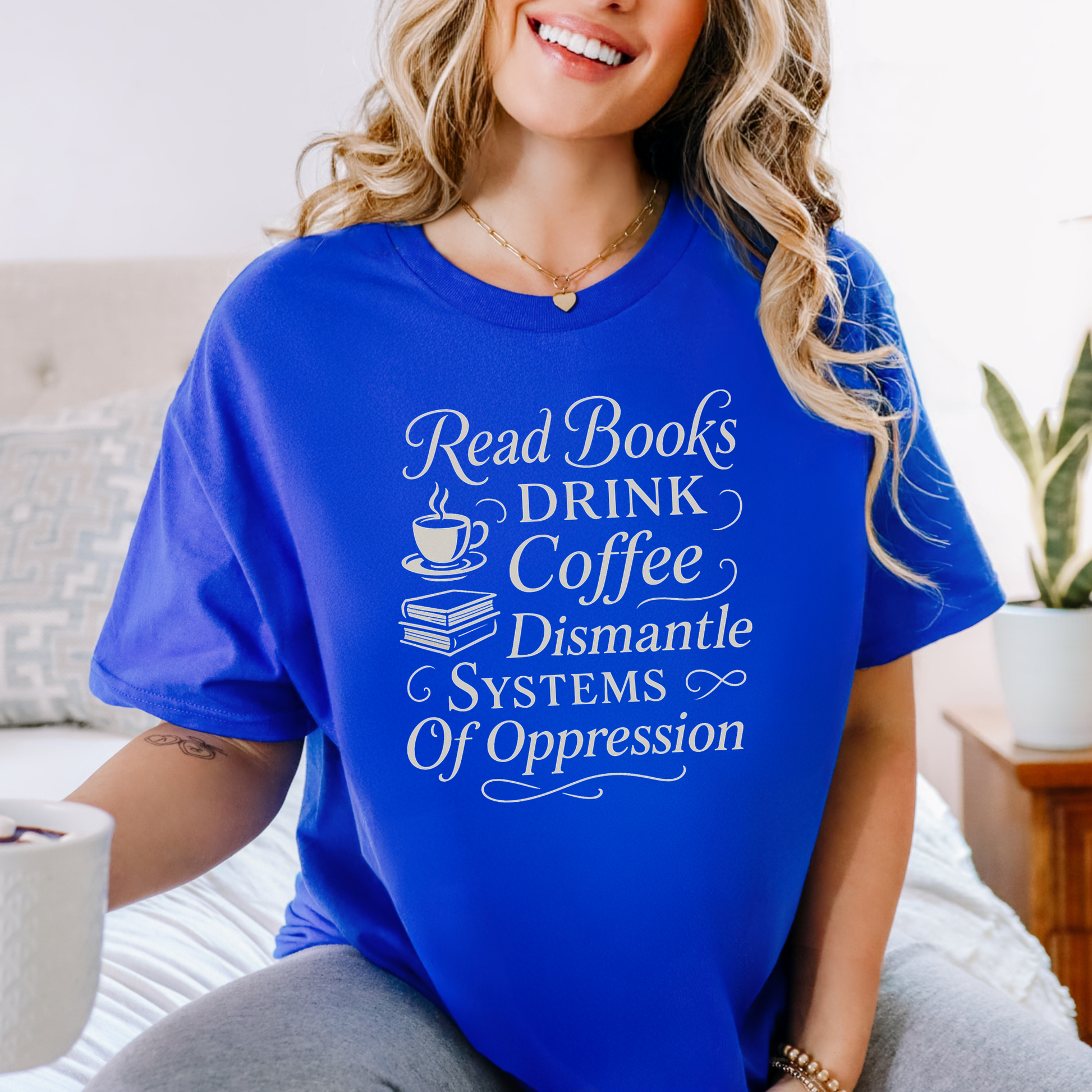 Woman wearing a blue t-shirt with motivational text, sitting on a couch. read books drink coffee dismantle systems of oppression shirt, activist shirt, book lover shirt, coffee lover tee, social justice shirt, political statement tee, feminist shirt, progressive apparel, reader shirt, library shirt, protest shirt, anti oppression shirt, unisex graphic tee, outspoken clothing, education and activism shirt