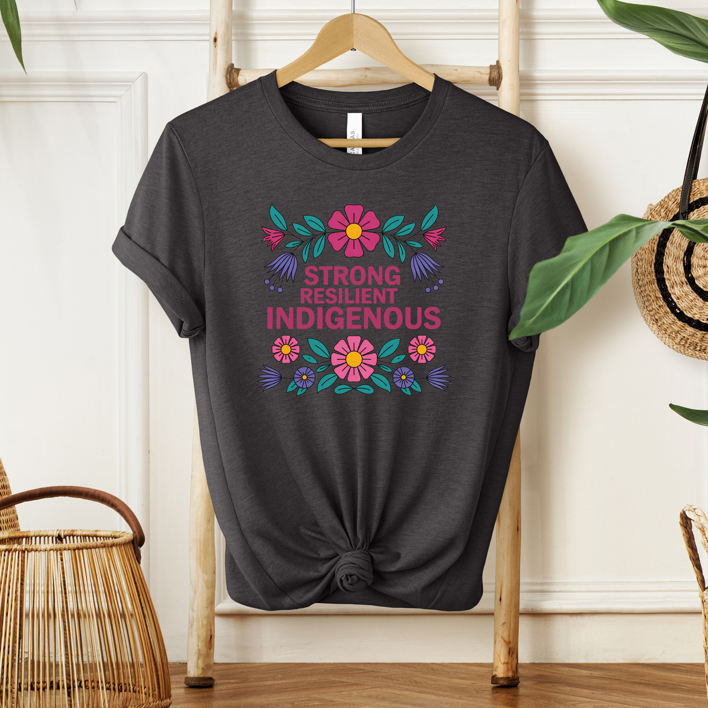 grey t-shirt with colorful floral design that says strong resilient indigenous, strong resilient indigenous t-shirt, indigenous floral tee, resilience graphic shirt, indigenous empowerment apparel, floral indigenous design, unisex indigenous shirt, sahdeh spruce clothing, indigenous pride t-shirt, native resilience tee, indigenous artist design, cultural strength shirt, heritage graphic apparel