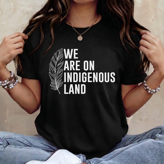 Person wearing a black t-shirt with 'We Are On Indigenous Land' text and a feather graphic. we are on Indigenous land, Indigenous land acknowledgement, Indigenous shirt, land back shirt, Indigenous awareness tee, unisex graphic tee, solidarity shirt, Indigenous pride, activist shirt, Native apparel, truth and reconciliation, awareness shirt, statement tee, Indigenous owned brand, cultural respect shirt