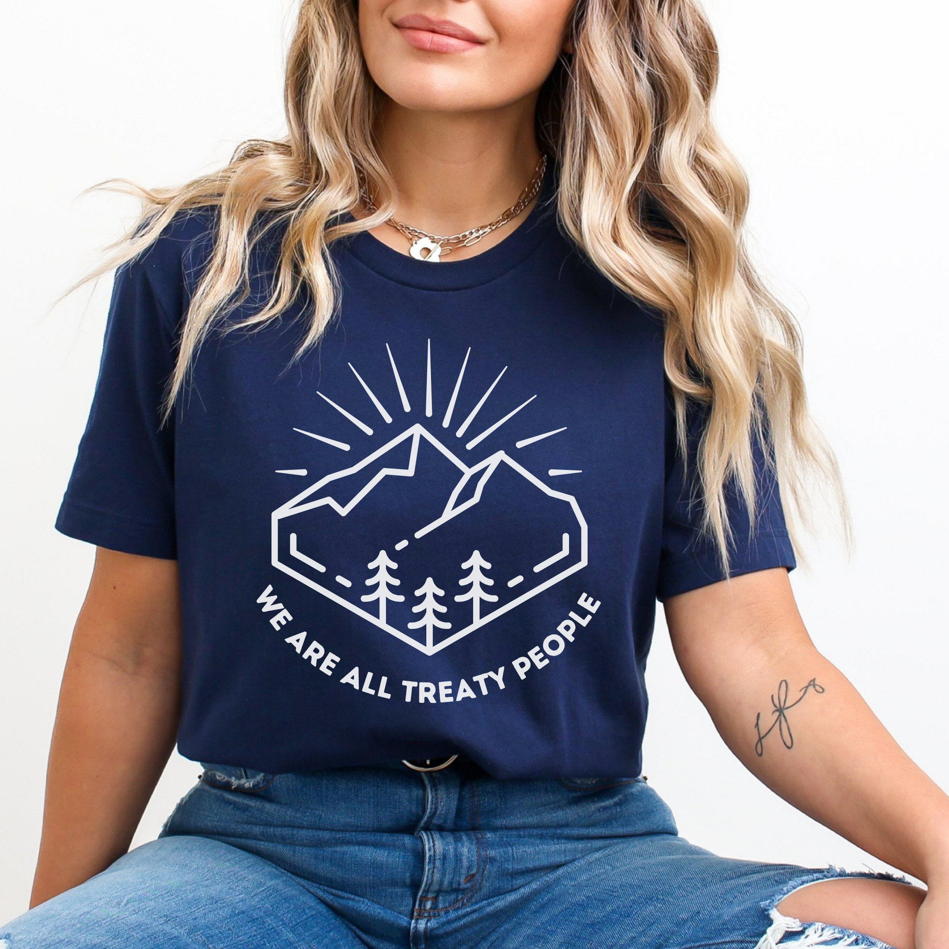 Person wearing a navy blue t-shirt with a mountain graphic and text. We Are All Treaty People, treaty shirt, Indigenous treaty awareness, Indigenous t shirt, unisex graphic tee, reconciliation shirt, Indigenous rights, awareness tee, activist shirt, Native apparel, solidarity shirt, truth and reconciliation, statement tee, Indigenous owned brand, educational shirt