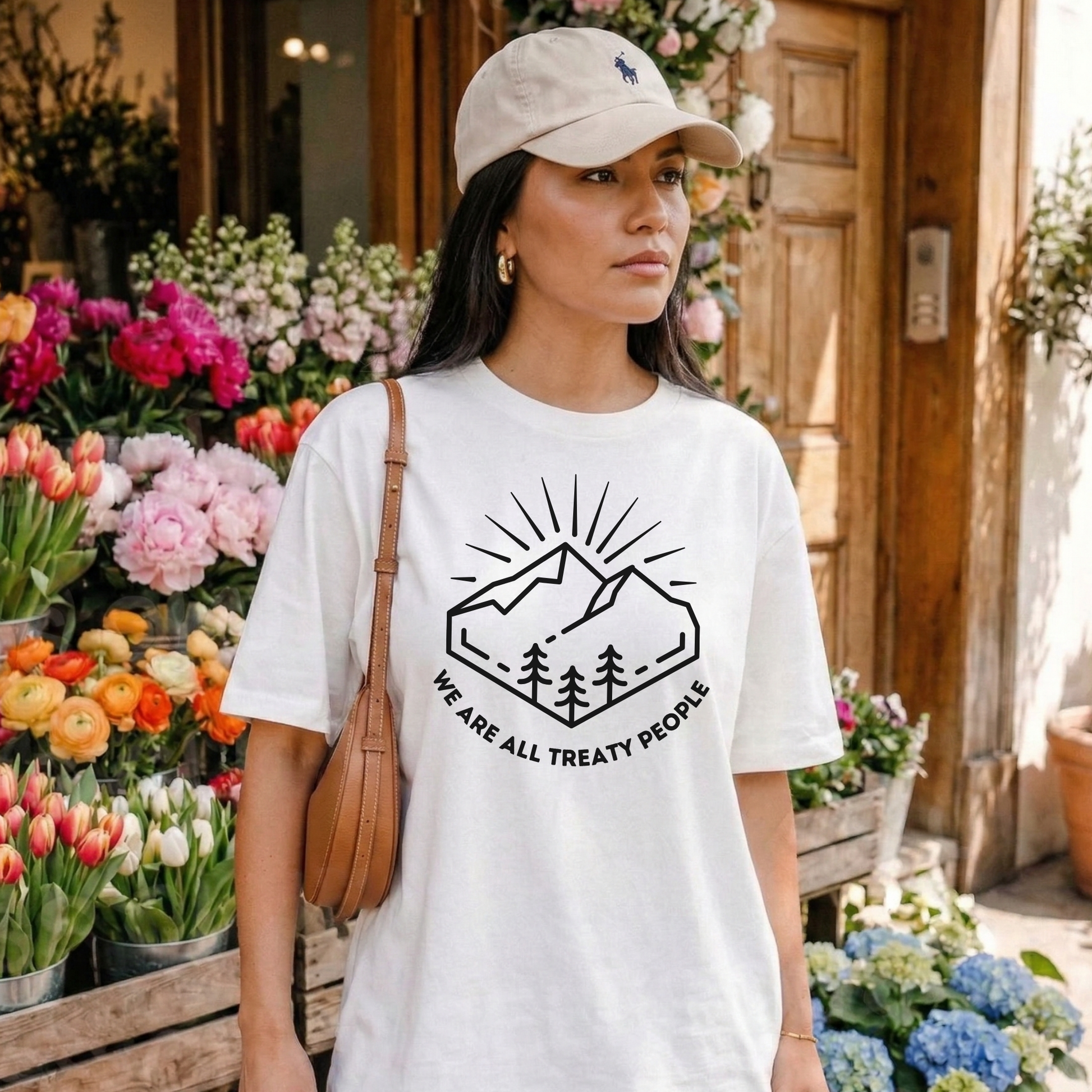 Woman wearing a white t-shirt with a graphic design and text, standing in front of a flower shop. We Are All Treaty People, treaty shirt, Indigenous treaty awareness, Indigenous t shirt, unisex graphic tee, reconciliation shirt, Indigenous rights, awareness tee, activist shirt, Native apparel, solidarity shirt, truth and reconciliation, statement tee, Indigenous owned brand, educational shirt