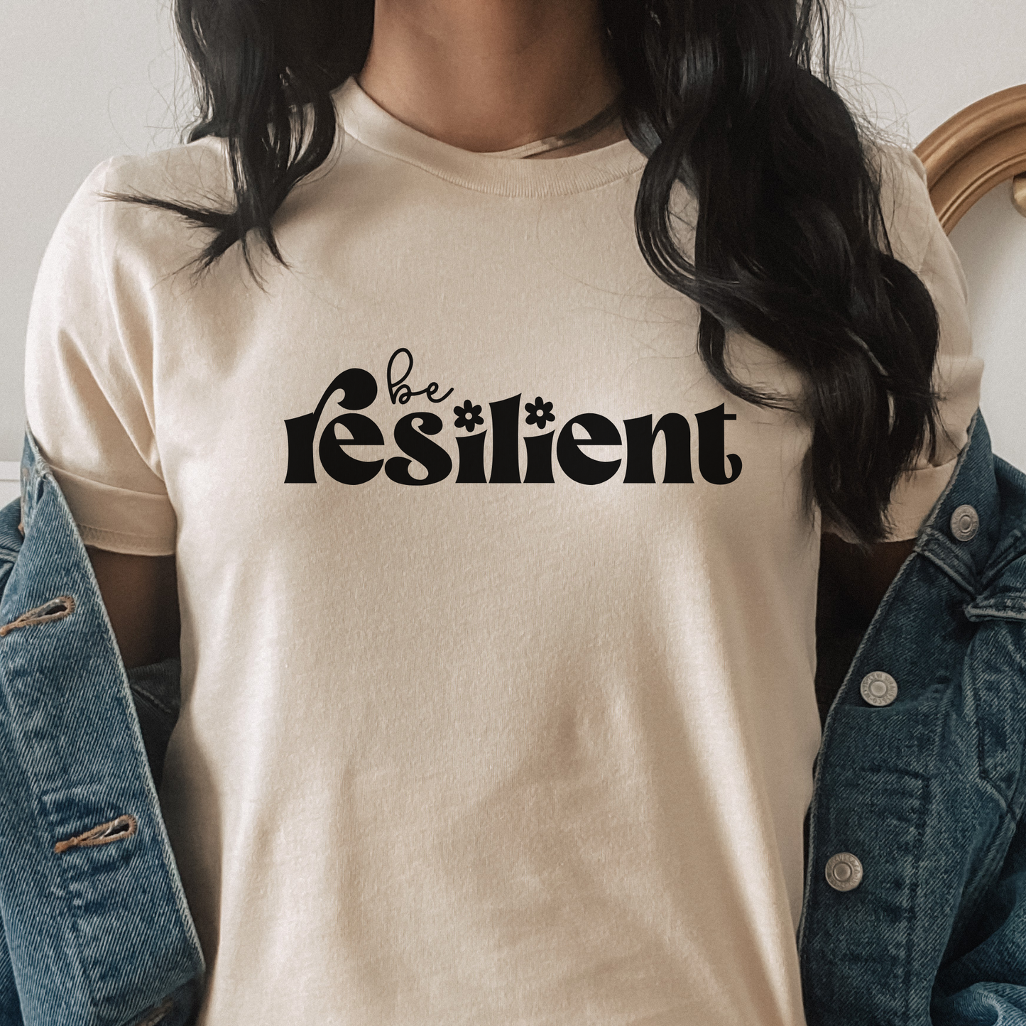 shirt with bold black retro typography that reads "Be Resilient" with subtle floral accents, symbolizing strength, perseverance, and personal growth. be resilient shirt, resilience t-shirt, motivational graphic tee, inspirational apparel, positive affirmation shirt, empowerment clothing, strength and perseverance shirt, mental wellness apparel, self growth clothing, motivational gift ideas, encouragement shirt, inspirational quote tee, positive mindset clothing, resilience gift, uplifting graphic shirt