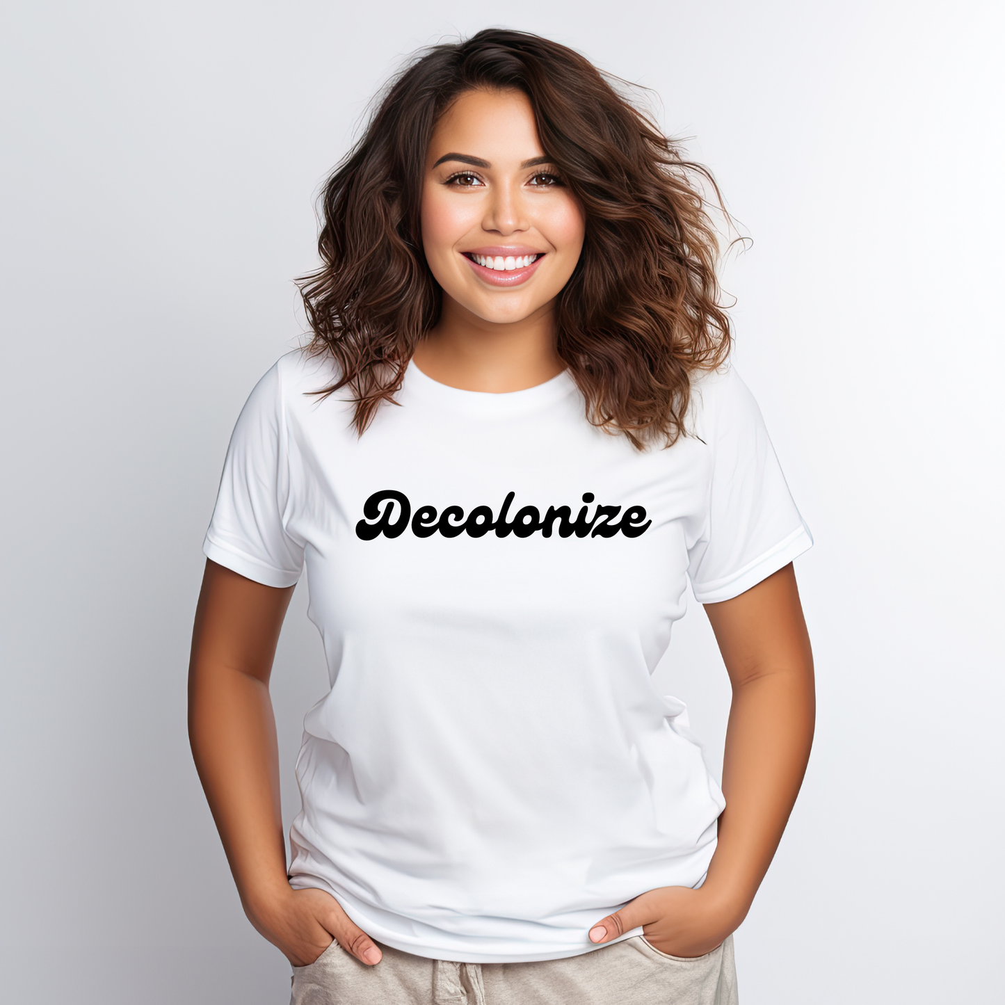 A smiling woman with wavy brown hair wearing a white crewneck t-shirt with the word 'Decolonize' printed in black script across the chest, set against a light gray studio background. decolonize shirt, truth and reconciliation shirt, indigenous shirt, decolonization apparel, indigenous ally shirt, social justice shirt, activist shirt, minimalist statement tee, indigenous owned, reconciliation shirt, education matters shirt, advocacy apparel, decolonize tee