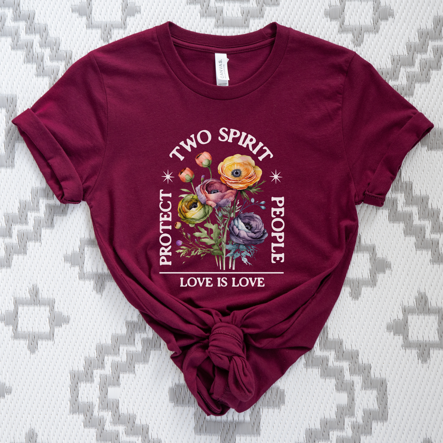 Maroon t-shirt with floral design and text on a patterned background protect two spirit people shirt, love is love two spirit tee, indigenous lgbtq shirt, two spirit pride t-shirt, indigenous pride apparel, lgbtq indigenous tee, two spirit advocacy shirt, love is love unisex tee, 2s pride shirt, indigenous lgbtq clothing, two spirit protection tee, queer indigenous apparel