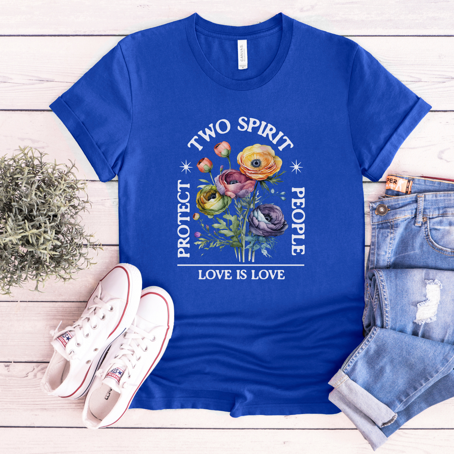 Blue t-shirt with 'Two Spirit People Love is Love' design on a wooden surface with shoes and jeans. protect two spirit people shirt, love is love two spirit tee, indigenous lgbtq shirt, two spirit pride t-shirt, indigenous pride apparel, lgbtq indigenous tee, two spirit advocacy shirt, love is love unisex tee, 2s pride shirt, indigenous lgbtq clothing, two spirit protection tee, queer indigenous apparel
