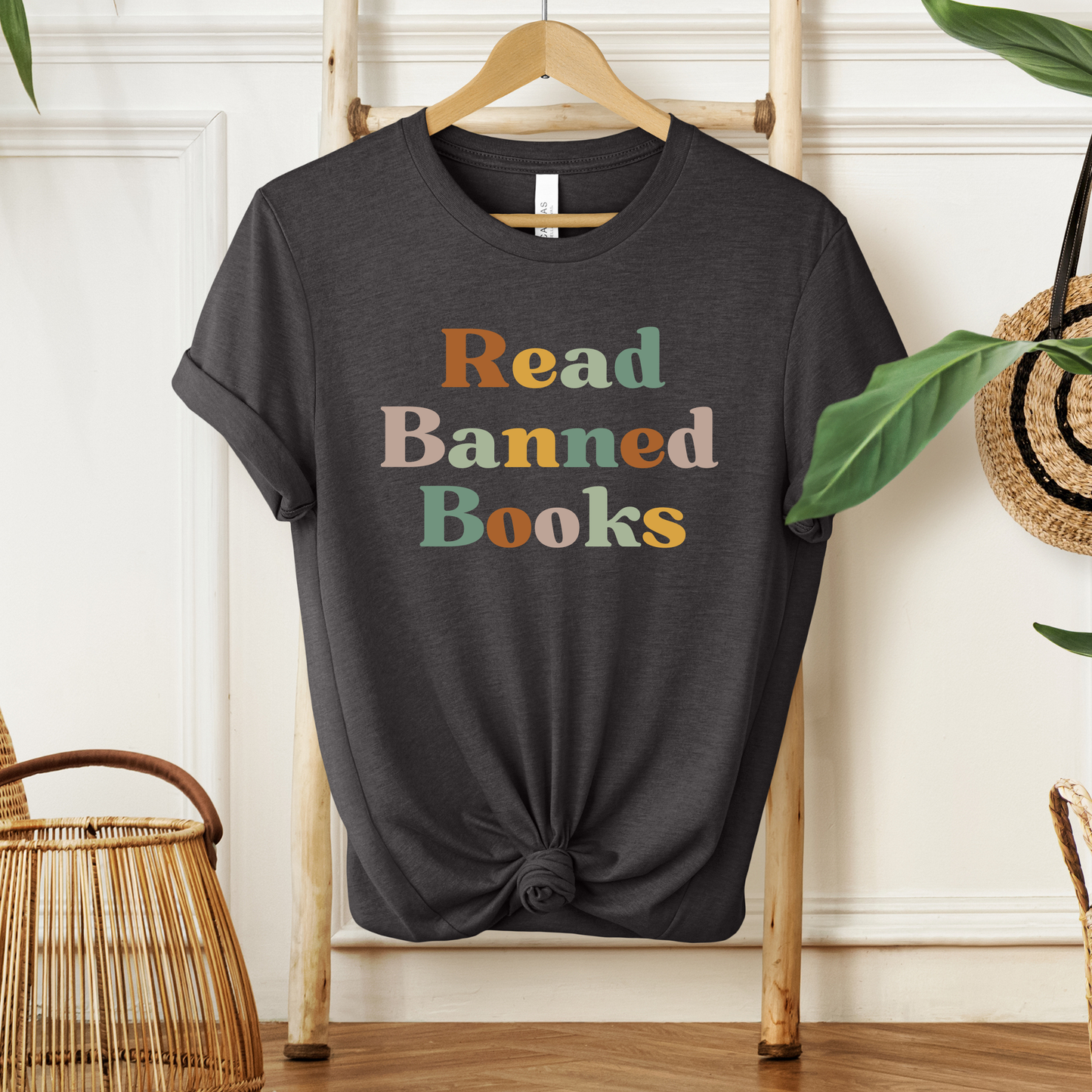 Black t-shirt with 'Read Banned Books' text on a wooden hanger against a white wall. read banned books shirt, banned books tee, book lover shirt, librarian shirt, teacher book shirt, freedom to read shirt, literary shirt, bookish apparel, reading shirt, library activism shirt, anti censorship shirt, intellectual freedom tee, book club shirt, educational shirt, reader gift shirt