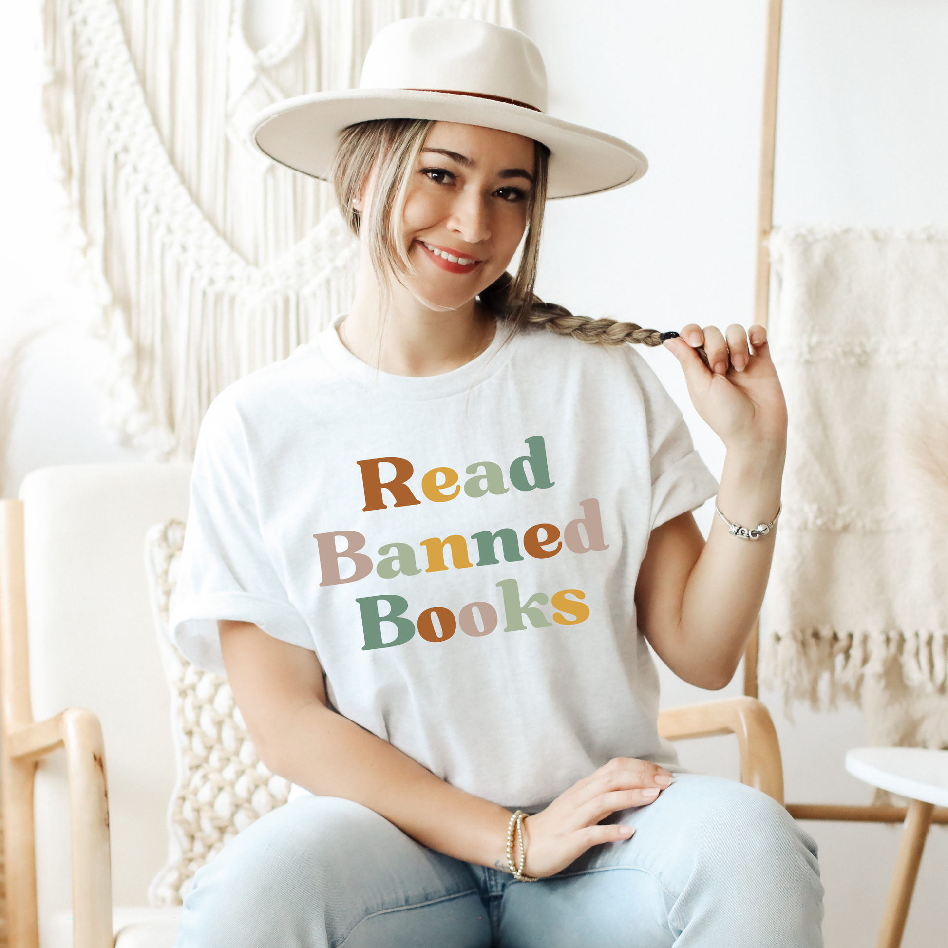 Person wearing a white t-shirt with 'Read Banned Books' text, sitting in a cozy room. read banned books shirt, banned books tee, book lover shirt, librarian shirt, teacher book shirt, freedom to read shirt, literary shirt, bookish apparel, reading shirt, library activism shirt, anti censorship shirt, intellectual freedom tee, book club shirt, educational shirt, reader gift shirt