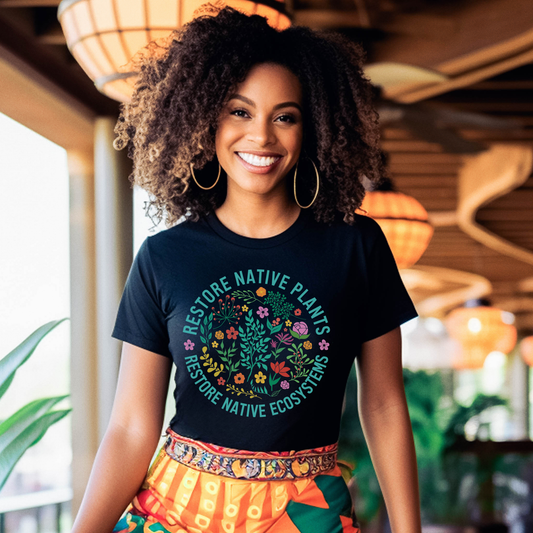 Woman wearing a black t-shirt with a nature-themed design and text, standing in an indoor setting. restore native plants shirt, native plants tee, indigenous plant shirt, land restoration shirt, plant lover tee, environmental advocacy shirt, native plant lover shirt, nature graphic tee, unisex plant shirt, eco friendly apparel, indigenous inspired shirt, stewardship t shirt