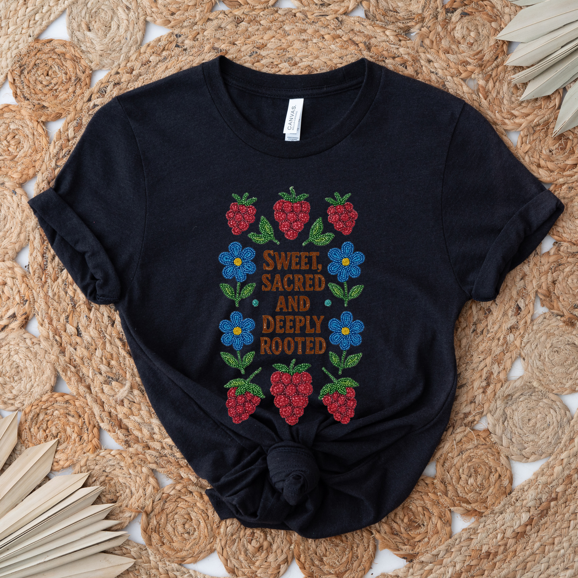 Black t-shirt with strawberry and flower design on a woven mat. sweet sacred deeply rooted shirt, beaded floral berry tee, indigenous beaded design shirt, sacred roots indigenous apparel, floral berry cultural t-shirt, original indigenous graphic tee, beaded indigenous shirt, deeply rooted heritage tee, unisex cultural pride shirt, sahdeh spruce indigenous design, berry beadwork t-shirt, ancestral connection apparel