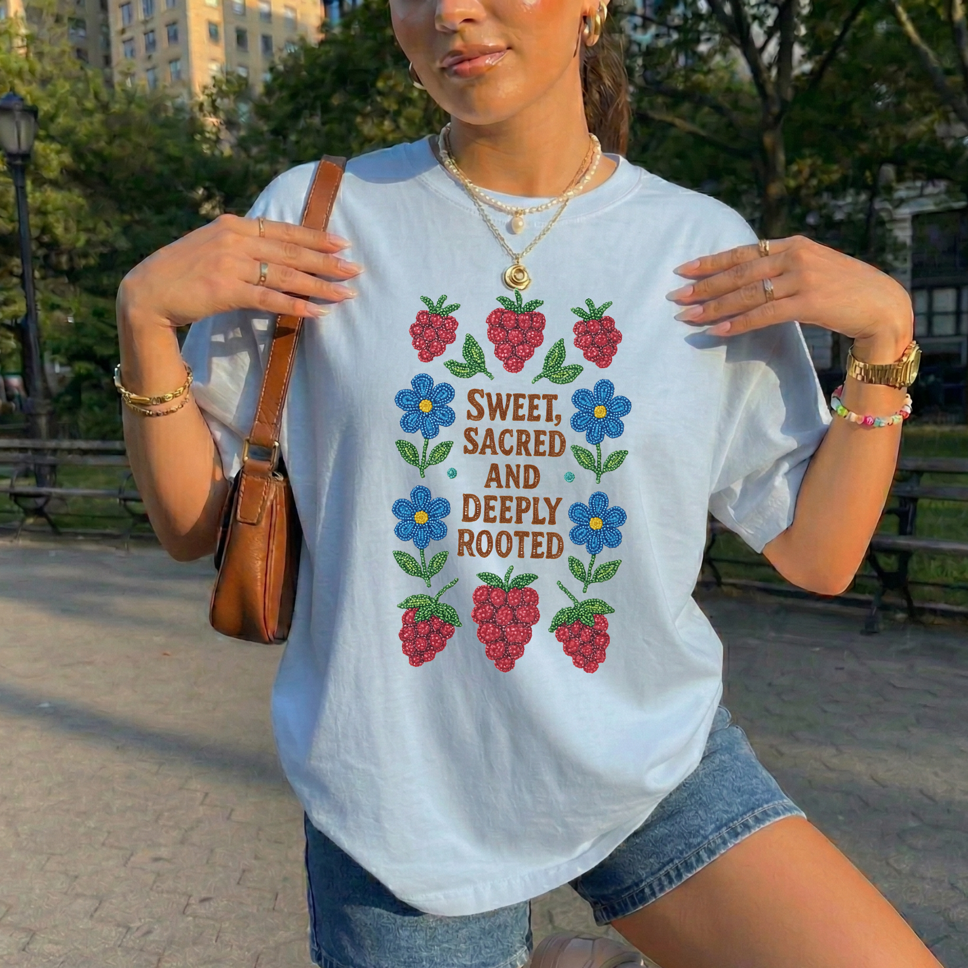 Person wearing a t-shirt with a colorful design and text in an outdoor setting sweet sacred deeply rooted shirt, beaded floral berry tee, indigenous beaded design shirt, sacred roots indigenous apparel, floral berry cultural t-shirt, original indigenous graphic tee, beaded indigenous shirt, deeply rooted heritage tee, unisex cultural pride shirt, sahdeh spruce indigenous design, berry beadwork t-shirt, ancestral connection apparel