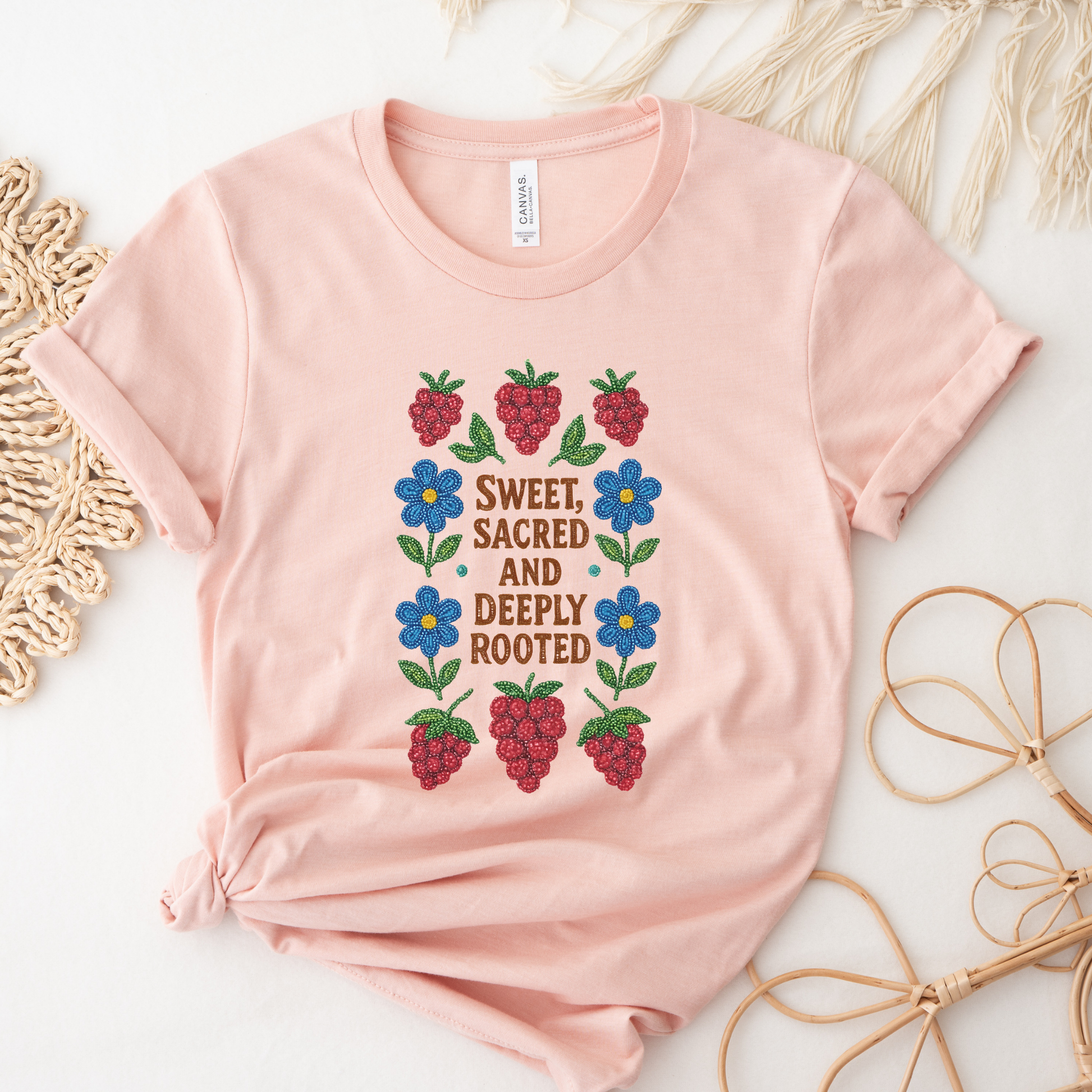 Pink t-shirt with floral and berry design on a textured surface sweet sacred deeply rooted shirt, beaded floral berry tee, indigenous beaded design shirt, sacred roots indigenous apparel, floral berry cultural t-shirt, original indigenous graphic tee, beaded indigenous shirt, deeply rooted heritage tee, unisex cultural pride shirt, sahdeh spruce indigenous design, berry beadwork t-shirt, ancestral connection apparel