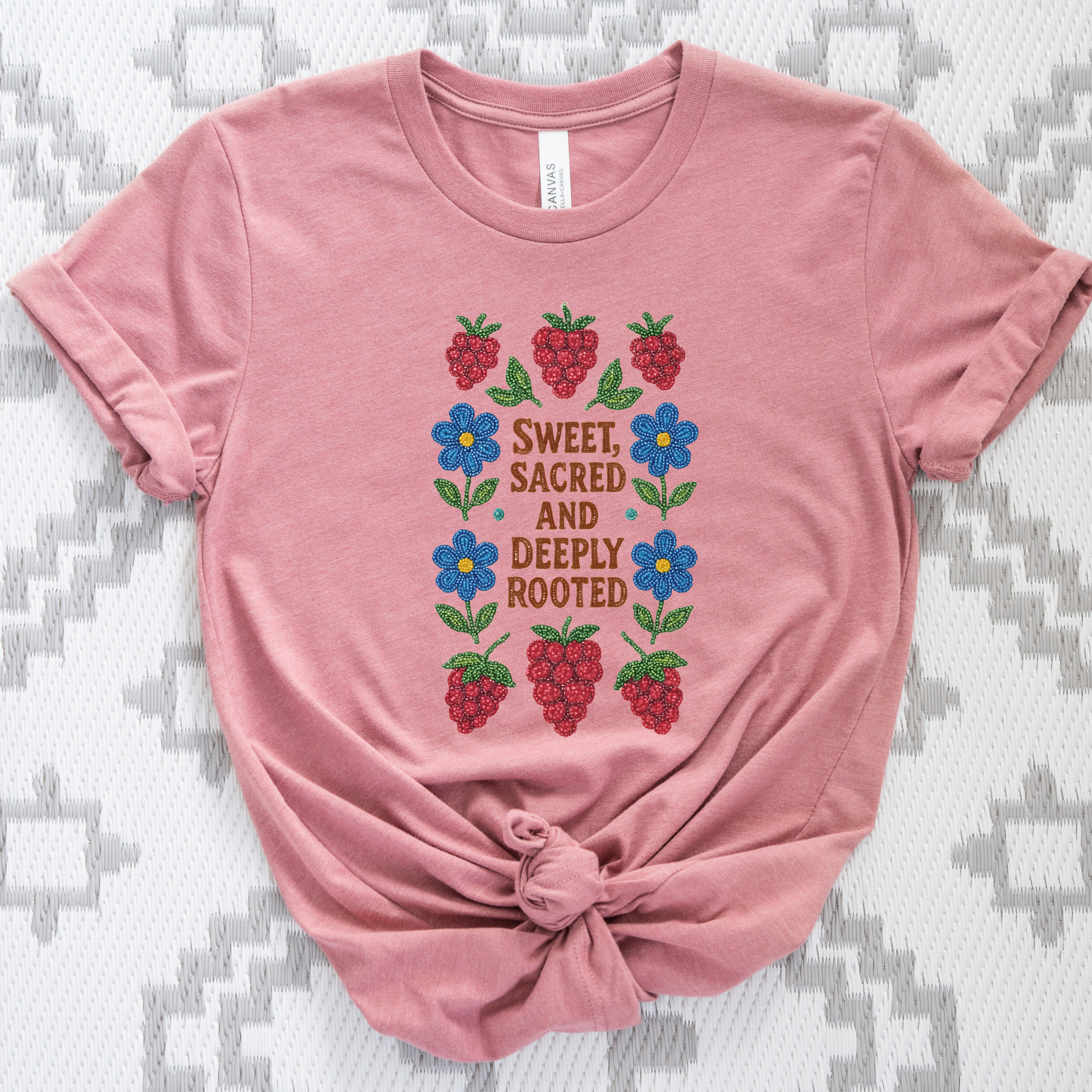 Pink t-shirt with floral and berry design on a textured surface sweet sacred deeply rooted shirt, beaded floral berry tee, indigenous beaded design shirt, sacred roots indigenous apparel, floral berry cultural t-shirt, original indigenous graphic tee, beaded indigenous shirt, deeply rooted heritage tee, unisex cultural pride shirt, sahdeh spruce indigenous design, berry beadwork t-shirt, ancestral connection apparel
